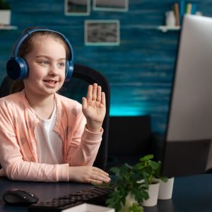 Smiling schoolkid wearing headset greeting remote teacher during online videocall meeting conference attenting to school lesson. Concept of distance education at home during coronavirus quarantine
